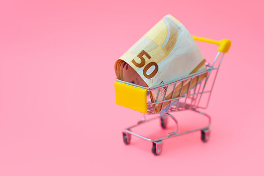 Euro banknote in shopping cart on pink background representing retail finance