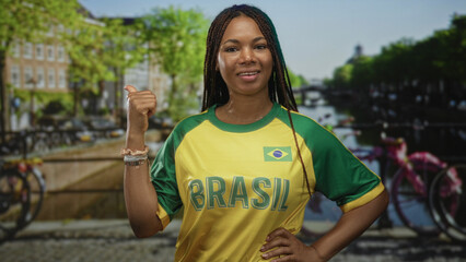 Naklejka premium Woman wearing brasil jersey gives thumbs up on street by a canal in amsterdam; pride travel support.