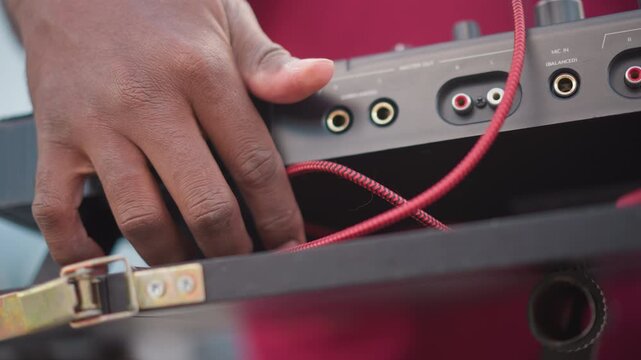 closeup audio jack and cable being plugged into portable mixer case by hand, braided red cable loops through metal latch, shallow depth of field, soft studio light, intimate tactile motion