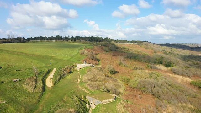 Aerial view of Omaha Beach and coastal cliffs in Normandy, France, featuring green fields, sandy shoreline, and World War II bunkers under a blue sky with clouds.