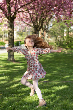 Girl with long hair spinning happily in park with pink sakura trees