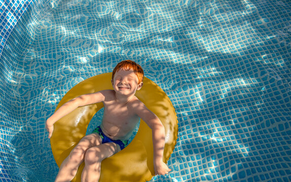 Cheerful red-haired child relaxing on yellow swimming ring in pool