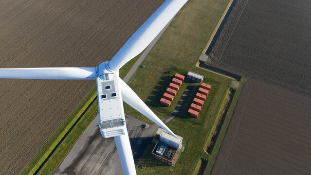 Aerial view of a colossal wind turbine casting a long shadow over the battery storage units, Middelharnis, South Holland, Netherlands.