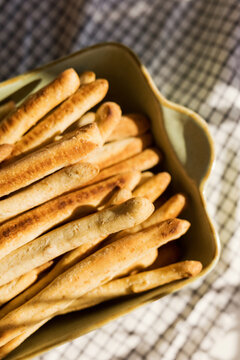 Fresh crispy sourdough grissini breadsticks in sunlight on checkered cloth