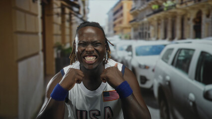 Fototapeta premium Man with bare arms raising fists and smiling on street wearing usa jersey; joy celebration energy optimism.