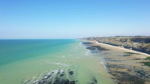 Scenic aerial view of the rugged coastline and turquoise waters near Port en Bessin, Normandy, France, under a clear blue sky.