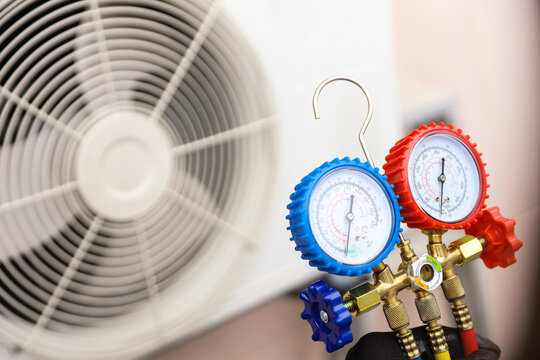 Air conditioning electrical technician using manifold gauge measuring tool checking refrigerant pump filling home air conditioner and maintenance heat fix repair and clean outdoor compressor unit.