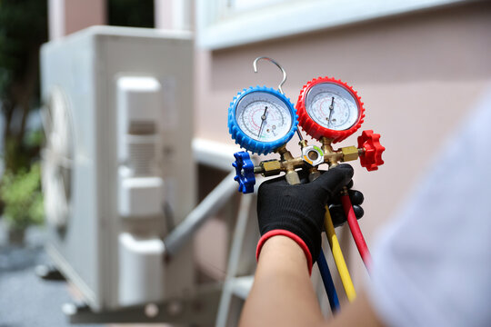 Air conditioning electrical technician using manifold gauge measuring tool checking refrigerant pump filling home air conditioner and maintenance heat fix repair and clean outdoor compressor unit.