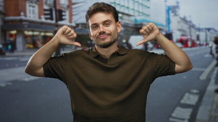 Fototapeta premium Man pointing thumbs to chest on busy city street near storefronts and blurred pedestrians; confidence pride self belief.