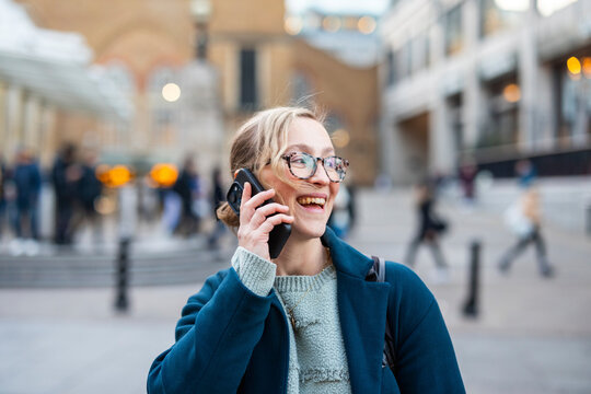 Woman smiling while talking on phone outdoors in a busy city street