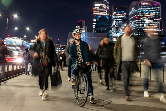 Cyclist commuting on London street at night among busy city crowd