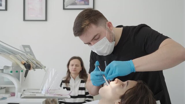 Male dental surgeon injects painkiller into child gum with carpal syringe before tooth extraction. Painless pediatric dentistry treatment involves local anesthesia numbing process.