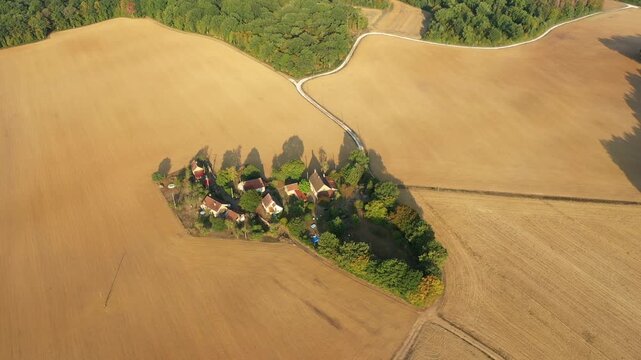 Drone shot of a cluster of traditional farm buildings surrounded by golden fields and trees in La Grange Treillard, France. The isolated property is set amidst expansive farmland and bordered by