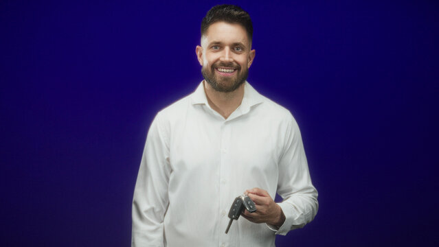 Hispanic man with beard holding car keys in hand and looking down in studio; pensive quiet reflection.