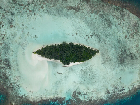 Aerial view of a small island covered in lush green trees surrounded by turquoise waters and white sandy beaches, Karimunjawa, Central Java, Indonesia.