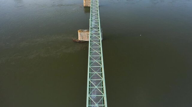 Drone shot of a metal bridge spanning the Loire River in Sully sur Loire, France. The structure crosses calm water, supported by stone pillars.