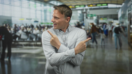 Man points index fingers both directions at airport signage while crossing arms and smiling, hands...