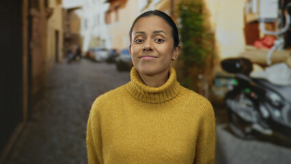 Woman smiling in a cozy yellow sweater stands confidently on an urban street, embodying tranquility and warmth in a rustic alley setting. © Krakenimages.com