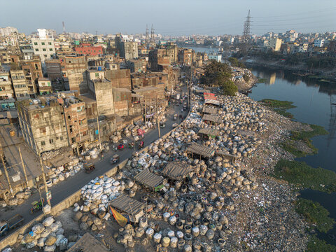 Aerial view of the stark contrast between the dense urban landscape and the heaps of plastic waste along the Buriganga River, Dhaka, Dhaka Division, Bangladesh.