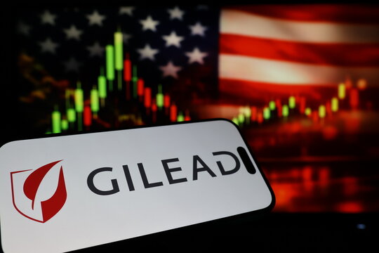 Kiel, Germany - 03-03-2026: US biotechnology company Gilead Sciences Inc. logo on smartphone against US flag and rising stock market candlestick chart concept