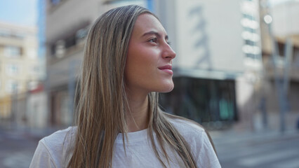 Young woman looking up on city street, face and bare neck visible, wearing white t shirt and gold hoop earring while standing near buildings  serenity. © Krakenimages.com