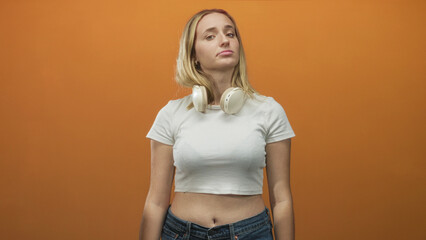 Woman wearing over ear headphones, pursed lips gesture and exposed navel in studio; indifference...