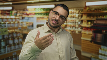 Obraz premium Man beckons with palm forward in a colorful supermarket building aisle filled with shelves; friendly invitation.