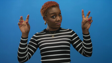 Obraz premium Woman in a black and white striped top showing air quotes with hands in a blue studio; sarcasm cynicism.