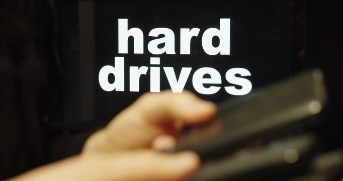 Close-up of a hand holding a hard drive in front of the words &ldquo;hard drives,&rdquo; representing data storage, backup solutions, and digital information technology.