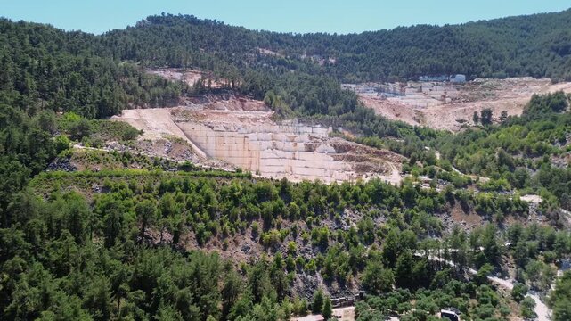 Cinematic drone shot over the famous snow white marble quarries of Thassos Greece featuring huge excavation terraces and the contrast between white stone and green pine forest.