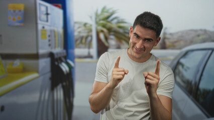 Fototapeta premium Man smiling and pointing finger toward camera at petrol pump beside silver car on street; confidence playful.
