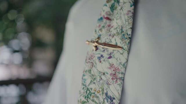 Close up of hand adjusting gold sword tie clip on floral tie