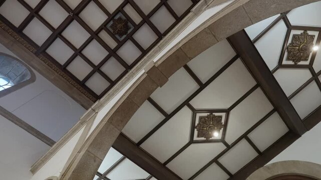 Upward angled view of church interior showing stone arch and geometric wooden coffered ceiling panels with decorative center detail