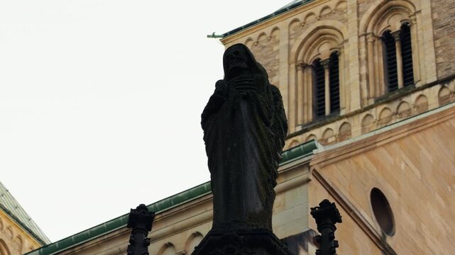 Dark stone statue depicting a skeletal figure in front of St Paulus Dom in M&uuml;nster, Germany. Gothic cathedral architecture and symbolic representation of death, faith and mortality.