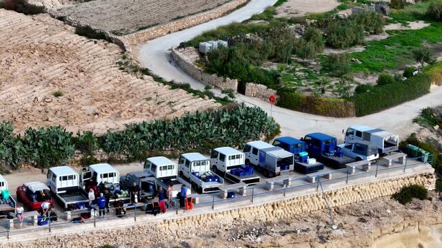 Divers Preparing for Underwater Exploration Along the Scenic Coastal Cliffs of Gozo Malta Under the Clear Mediterranean Summer Sky with Bright Blue and White Trucks Parked on the High Vantage Point