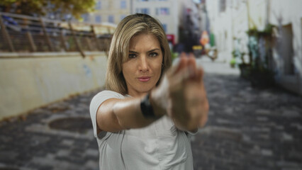 Fototapeta premium Woman with hands clasped into a finger gun gesture on a cobblestone street in an urban alley; determination.