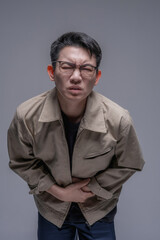 Fototapeta premium Asian man suffering from stomach pain holding abdomen, digestive problem and gastritis concept, healthcare and illness theme, adult male with glasses feeling abdominal ache, studio portrait isolated b