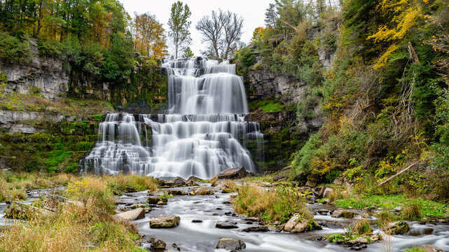 Chittenango Falls main cascade in Chittenango Falls State Park, New York, where water drops over 400‑million‑year‑old Devonian bedrock into a forested gorge with autumn foliage and a rocky streambed.