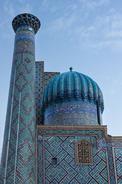 Sher Dor Madrasah turquoise dome and azure minaret fragment. Intricate mosaic tiles, geometric patterns, calligraphy bands and ribbed cupola under blue sky. Registan Square, Samarkand, Uzbekistan.