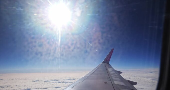 Timisoara, Romania - February 24, 2026: Airplane wing against bright sun and blue sky, showcasing clouds below in a clear atmosphere during flight