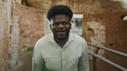 Obraz premium Man smiling with eyes closed and open mouth, wearing linen shirt and standing on a walkway by a railing in roman ruins building; joy wonder.