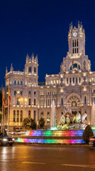 Fototapeta premium Night view of detailed white building with clock tower and fountain with colored lights, representing urban architecture, tourism, and travel destination