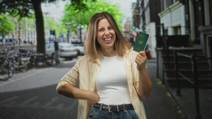 Fototapeta premium Woman holding passport up, hand on hip, smiling and looking sideways in street with bicycles and buildings; joy travel freedom.