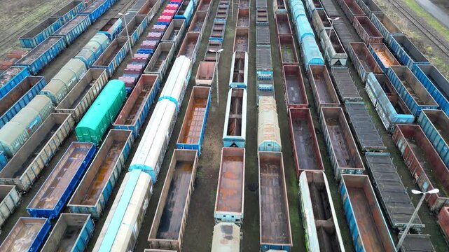 Aerial view of a vast freight train yard showcasing rows of colorful train cars, with a gradual zoom out revealing the expansive layout and intricate details of the scene