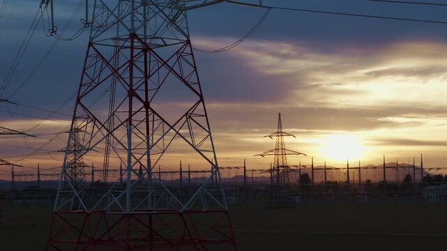 View of a high voltage electrical substation switchyard with transformers and transmission lines in a rural location during sunset.
