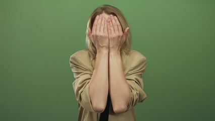 Blonde woman smiles playfully against green background, covering and uncovering her face while...