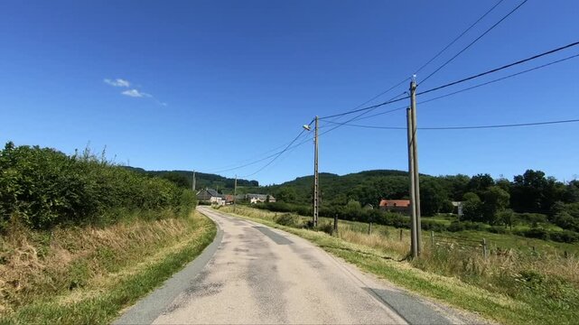 Scenic country road leading to a small village in the Morvan region of France, surrounded by lush greenery and hills under a clear blue sky.