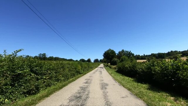 Empty country road surrounded by lush greenery and trees under a clear blue sky in the Morvan region of France. Peaceful rural landscape ideal for travel and nature concepts.