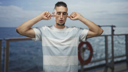 Man plugs ears with fingers on ship deck by lifebuoy and metal railing, eyes closed in light...