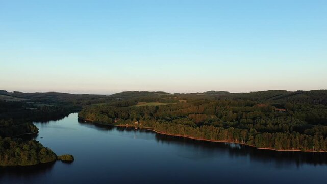 Scenic aerial panorama of Lac des Settons surrounded by lush green forest under a clear sky during sunset in Burgundy, France.